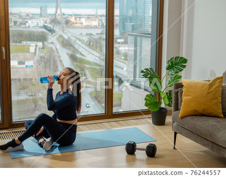 Sportive lady with ponytail in tracksuit drinks water on mat Sportive lady with ponytail in tracksuit drinks water on mat 76244557