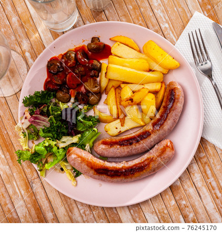 Fried sausages with baked potatoes, mushrooms and lettuce 76245170
