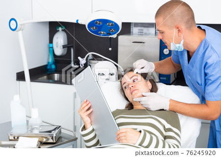 Cosmetologist examining female client face before procedure 76245920