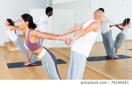 Women and men performing paired yoga exercises during group training Women and men performing paired yoga exercises during group training 76246061