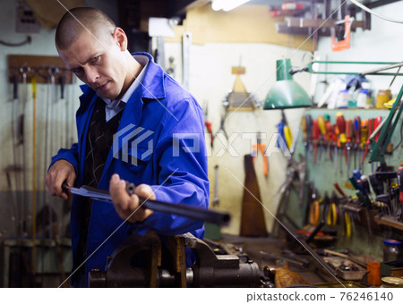 Skilled craftsman of weapons workshop cleaning rifle barrel with ramrod 76246140