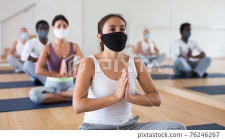 Hispanic woman in protective mask practicing yoga postures at gym 76246267