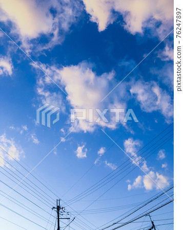 Utility poles and power lines with clear blue sky and white clouds in the background 76247897