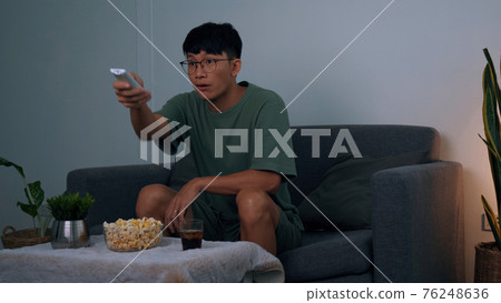 Asian guy is relaxing for the weekend by watching series his home at night. 76248636