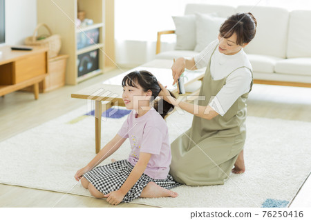 Girl having her mother brush her hair 76250416