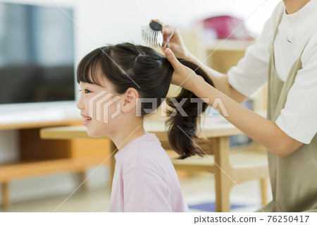 Girl having her mother brush her hair 76250417