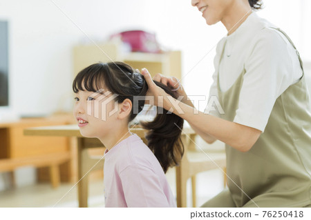 A girl who has her mother tie her hair 76250418