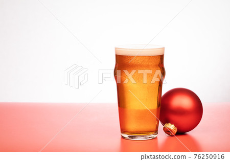 Pint glass of ale or beer with christmas bauble on red background Pint glass of ale or beer with christmas bauble on red background 76250916
