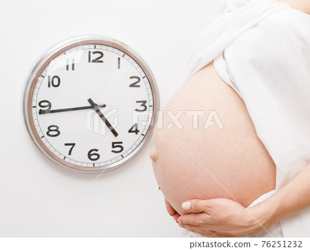 Pregnant woman with clock on a wall during final weeks of pregnancy Pregnant woman with clock on a wall during final weeks of pregnancy 76251232