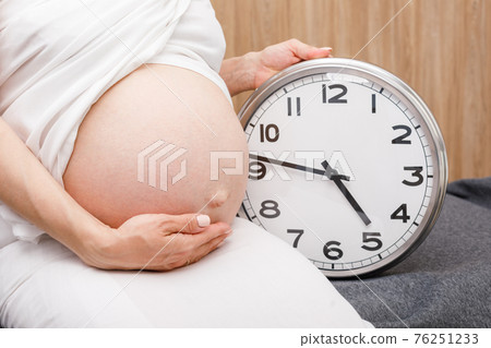Pregnant woman with clock during final weeks of pregnancy 76251233
