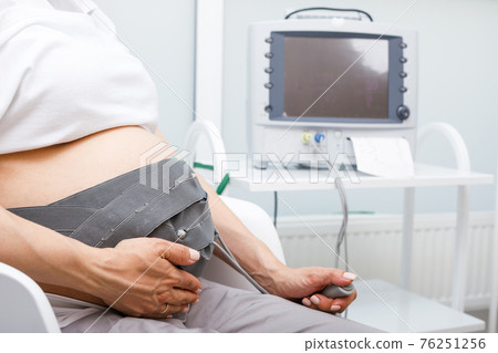 Pregnant woman performing cardiotocography or CTG monitoring fetal heartbeat and uterine contractions during final weeks of pregnancy Pregnant woman performing cardiotocography or CTG monitoring fetal heartbeat and uterine contractions during final weeks of pregnancy 76251256