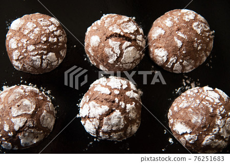Cracked chocolate cookies with icing sugar on a pan 76251683