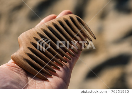 Wooden comb on a palm at sand background. Tool for scalp massage and aroma combing. Hair care concept. Wooden comb on a palm at sand background. Tool for scalp massage and aroma combing. Hair care concept. 76251920