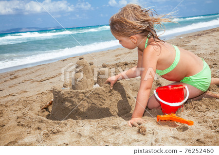 Girl building a sandcastle on a beach 76252460
