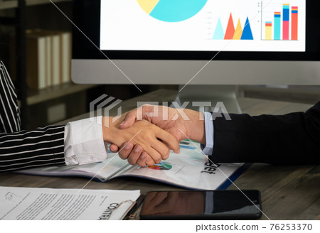 Businesswomen seated at office desk shaking hands with businessman after signed contract. Businesswomen seated at office desk shaking hands with businessman after signed contract. 76253370