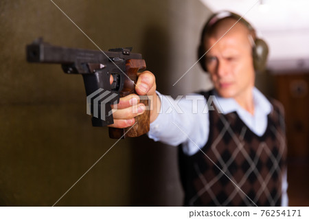 Hand of shooter squeezing pistol grip and pressing trigger at firing range Hand of shooter squeezing pistol grip and pressing trigger at firing range 76254171
