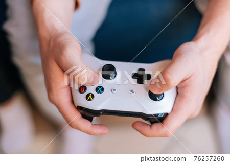 Top close-up view of unrecognizable man holding joystick and playing video games on console at home with friends.  76257260