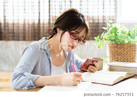 Young woman with glasses checking smartphone videos while studying 76257351