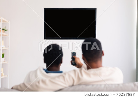 Black couple watching TV with mockup and using remote controller Black couple watching TV with mockup and using remote controller 76257687