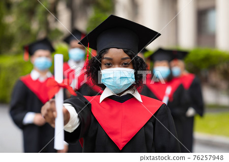 African american young lady in graduation costume and face mask 76257948