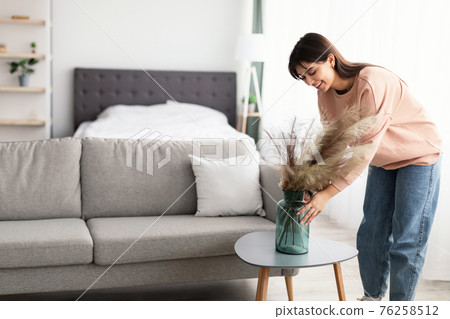 Woman putting vase with white dried pampas grass on table Woman putting vase with white dried pampas grass on table 76258512