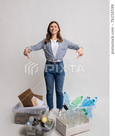 Young lady sorting waste, pointing at containers with different kind of garbage 76258599