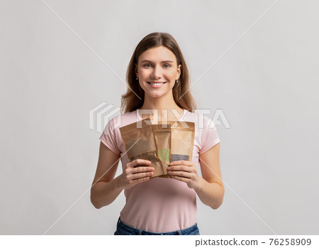 Eco Storage Concept. Smiling millennial lady holding doypack bags with weight groceries Eco Storage Concept. Smiling millennial lady holding doypack bags with weight groceries 76258909