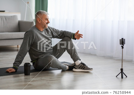 Handsome senior man fitness coach broadcasting from home Handsome senior man fitness coach broadcasting from home 76258944