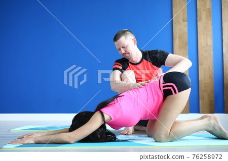 Male trainer helps woman to do exercises for spine 76258972