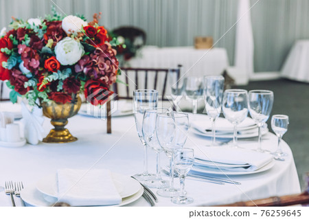 Fancy table set for dinner with flower composition in restaurant, luxury interior background. Wedding elegant banquet decoration and items for food arranged by catering service on white table. Fancy table set for dinner with flower composition in restaurant, luxury interior background. Wedding elegant banquet decoration and items for food arranged by catering service on white table. 76259645