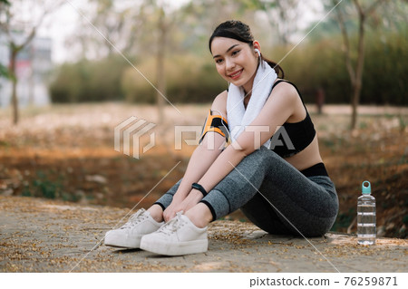 Athletic asian woman resting after a hard training in the mountains at sunset. Sport tight clothes 76259871