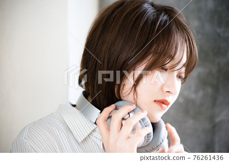 A woman who takes off her headphones and wears it around her neck 76261436