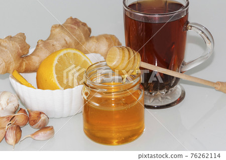 Honey and pieces of garlic on the background of honeycomb. Honey in a glass jar and honeycomb. Honey and pieces of garlic on the background of honeycomb. Honey in a glass jar and honeycomb. 76262114