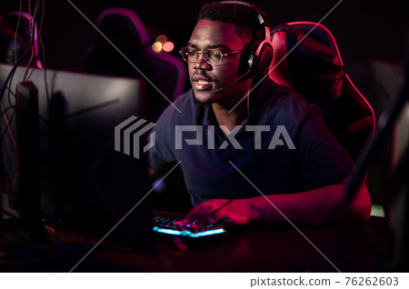 An african student sits in a gaming chair in a computer club, puts on headphones, smiles, and prepares for the game An african student sits in a gaming chair in a computer club, puts on headphones, smiles, and prepares for the game 76262603