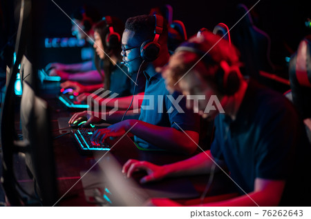 A multi-racial team of esports athletes conducts a training session before an online shooter tournament. Neon light. 76262643