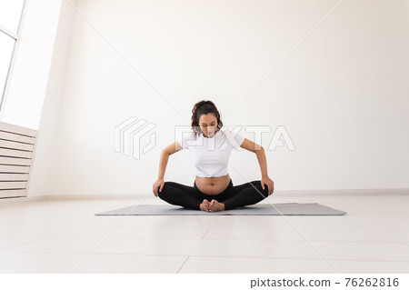 Purposeful pregnant woman exercises during yoga class and relaxes while sitting on a mat on the floor. Concept of physical and mental preparation of the body for childbirth. Place for text Purposeful pregnant woman exercises during yoga class and relaxes while sitting on a mat on the floor. Concept of physical and mental preparation of the body for childbirth. Place for text 76262816