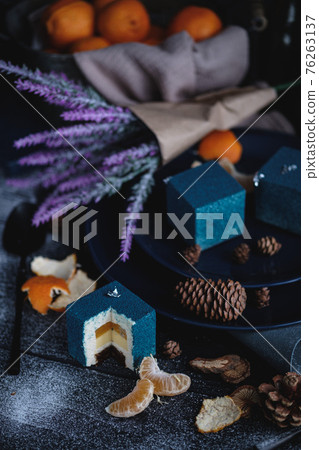 Blue cake filled with orange and tangerine in the shape of a cube. Nearby on a black table are ingredients oranges, tangerines, nuts. Rustic style Blue cake filled with orange and tangerine in the shape of a cube. Nearby on a black table are ingredients oranges, tangerines, nuts. Rustic style 76263137