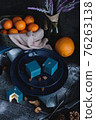 Blue cake filled with orange and tangerine in the shape of a cube. Nearby on a black table are ingredients oranges, tangerines, nuts. Rustic style 76263138