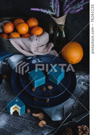 Blue cake filled with orange and tangerine in the shape of a cube. Nearby on a black table are ingredients oranges, tangerines, nuts. Rustic style Blue cake filled with orange and tangerine in the shape of a cube. Nearby on a black table are ingredients oranges, tangerines, nuts. Rustic style 76263138
