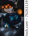 Blue cake filled with orange and tangerine in the shape of a cube. Nearby on a black table are ingredients oranges, tangerines, nuts. Rustic style 76263139