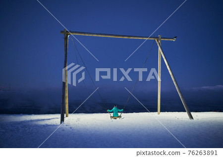 Playground swing with thick snow on ground and views of mountain and cloudy sky. Playground swing with thick snow on ground and views of mountain and cloudy sky. 76263891