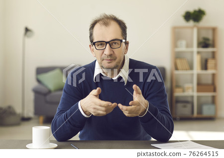 Portrait of mature man sitting at desk with laptop looking pointing to camera 76264515