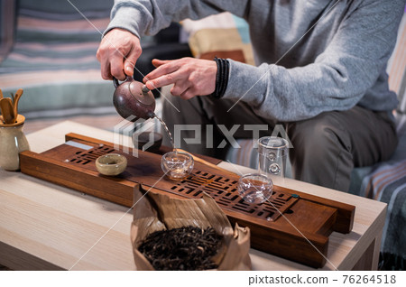 The master of tea ceremonies pours amber tea in a thin stream into tasting cups. Close-up with a blurry background. 76264518