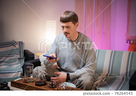 A man photographs a set for a tea ceremony on a smartphone camera for his blog on the social network at home. A man photographs a set for a tea ceremony on a smartphone camera for his blog on the social network at home. 76264543