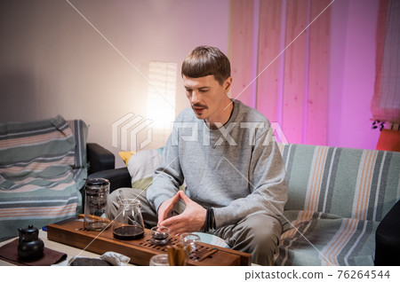 A young adult man learns the art of meditation during a tea ceremony to relax and enjoy the natural aroma of chinese black raw tea. A young adult man learns the art of meditation during a tea ceremony to relax and enjoy the natural aroma of chinese black raw tea. 76264544