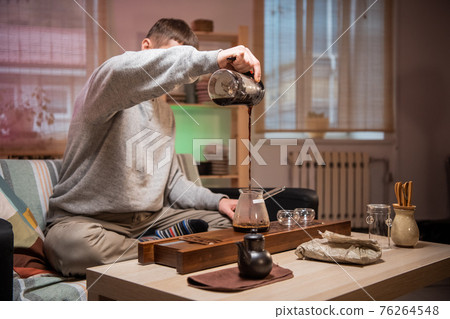 The process of brewing authentic japanese tea at home. A man pours hot water into a bowl with dried tea leaves. 76264548