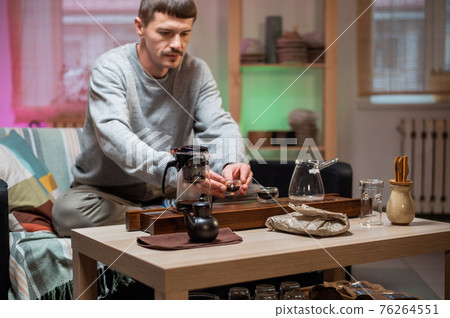 A man brews chinese tea according to an old oriental recipe on a bamboo gongfu tray. Adds boiling water from the teapot to the teacup. A man brews chinese tea according to an old oriental recipe on a bamboo gongfu tray. Adds boiling water from the teapot to the teacup. 76264551