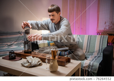 A young man is introduced to the Chinese culture of tea drinking. Brews fragrant raw tea at home. Pour boiling water over tea leaves. 76264552