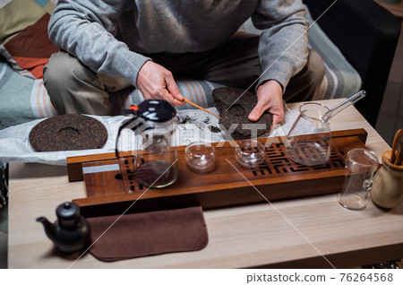 Close up. A tea seller breaks off a piece of strong black tea with a tea needle for sale in a tea shop. 76264568