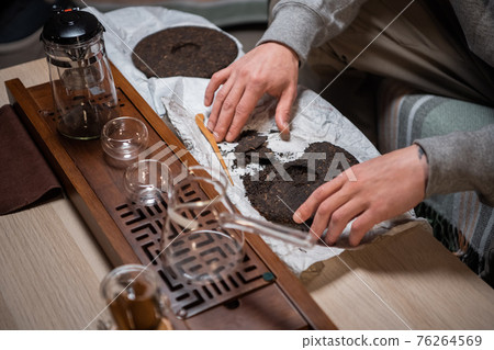 A man bought a set of milking tea ceremony at home and breaks off a piece of raw puerh tea cake with a needle to brew a strong fragrant tea. A man bought a set of milking tea ceremony at home and breaks off a piece of raw puerh tea cake with a needle to brew a strong fragrant tea. 76264569